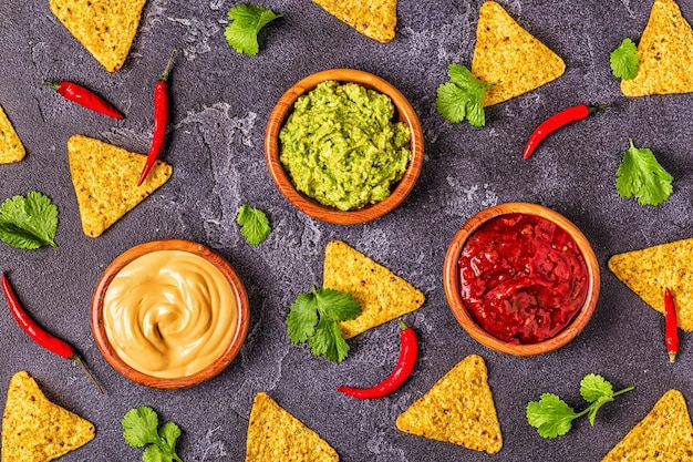 Mexican food background: guacamole, salsa, cheesy sauces with ingredients on black background, top view.