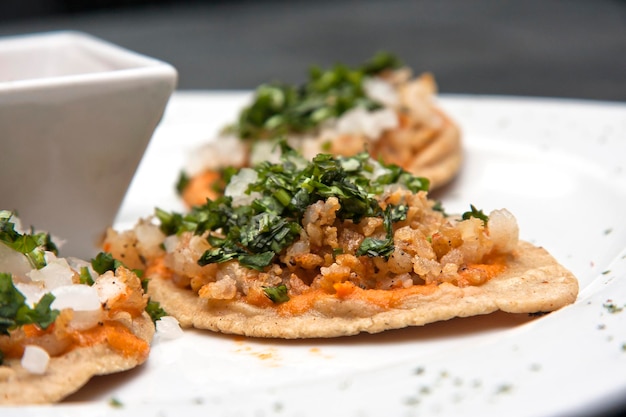 Mexican food, Chalupas or sope with chicharrón shrimp, hot sauce, cilantro and onion, white plate