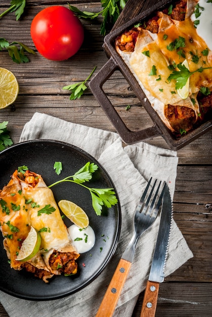 Mexican food. Cuisine of South America. Traditional dish of spicy beef enchiladas with corn, beans, tomato. On a baking tray, on old rustic wooden background. Copy space top view