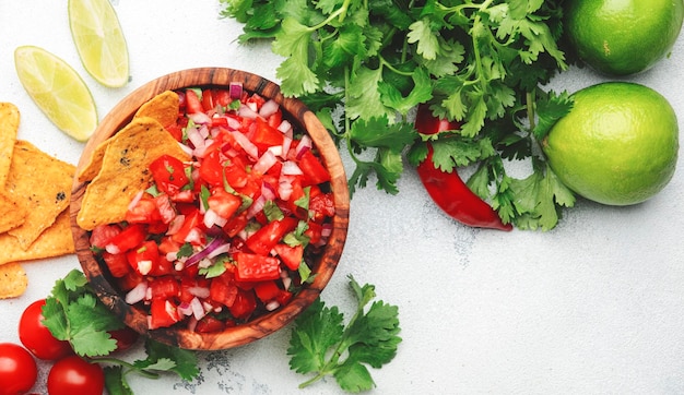 Mexican food Spicy salsa sauce with tomatoes chili peppers onion garlic and cilantro with nachos corn chips white table background top view