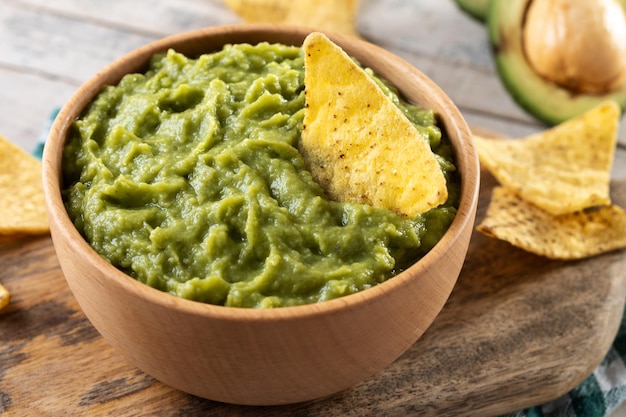 Mexican guacamole with nacho chip in wooden bowl on rustic wooden table Top view Traditional mexican food