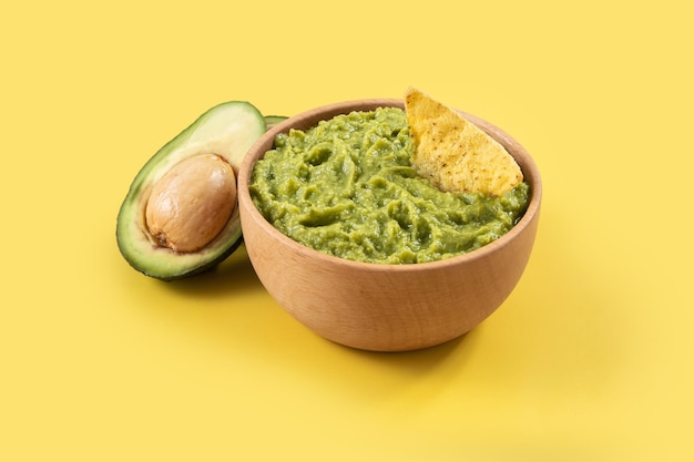 Mexican guacamole with nacho chip on yellow background