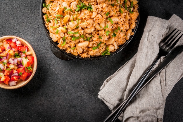 Mexican, Latin American cuisine. Mexican Rice and Beans Bowl- recipe made with rice and white beans, homemade, with fresh herbs and herbs. In a frying pan for cooking, with salsa, top view copyspace