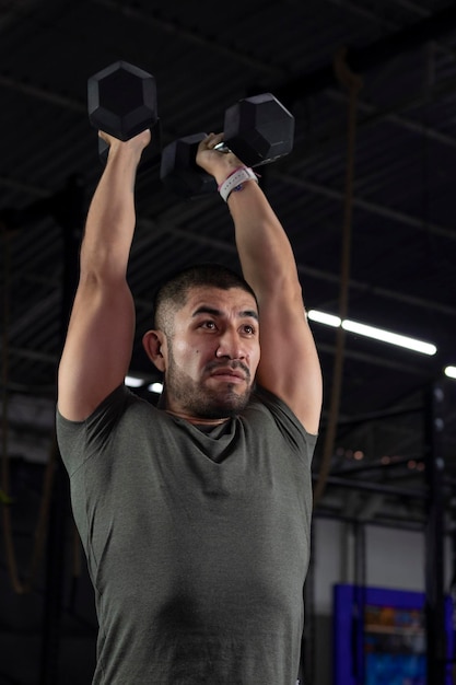 Mexican man in sportswear exercising in a gym using two dumbbells