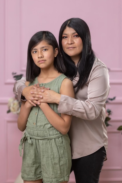 Mexican mother and daughter hugging on pink background isolated