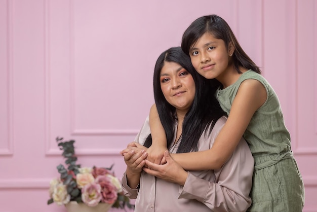 Mexican mother and daughter hugging on pink background isolated