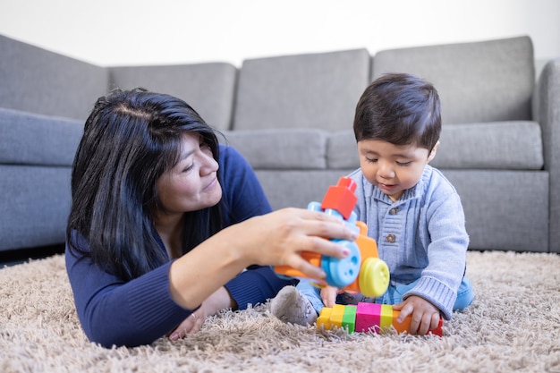 Mexican mother playing with son on carpet at home