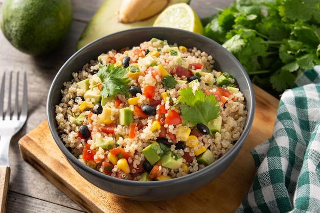 Mexican salad with quinoa in bowl on wooden table.