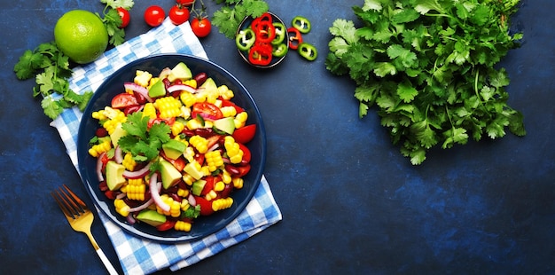 Mexican spicy salad with corn red beans avocado jalapeno peppers cherry tomatoes onion and cilantro Blue table background top view