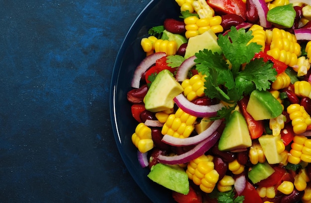 Mexican spicy salad with corn red beans avocado jalapeno peppers cherry tomatoes onion and cilantro Blue table background top view