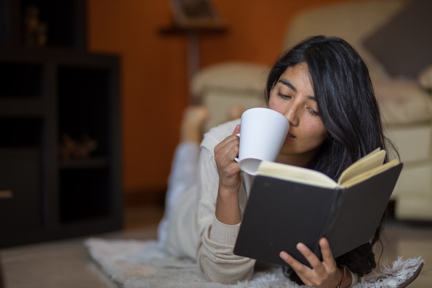 Mexican woman  lying down looking at the side with book with cup of coffee