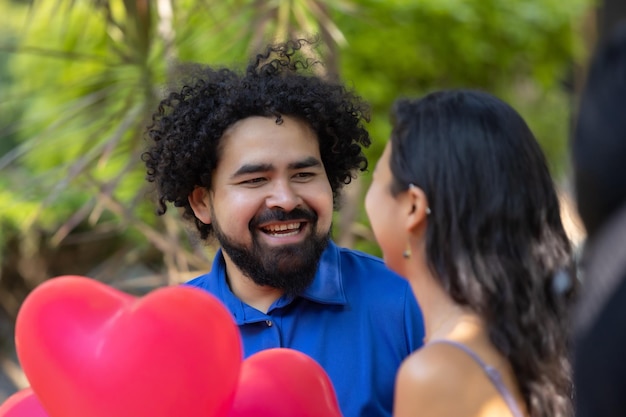 Mexican young latin couple laughing and talking on valentine's day with red heart shaped balloons