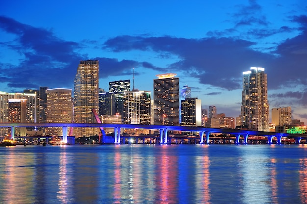 Miami city skyline panorama at dusk with urban skyscrapers and bridge over sea with reflection