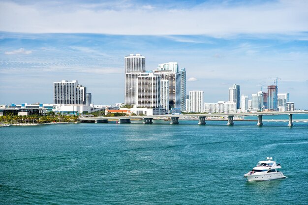 Miami skyscrapers with blue cloudy sky boat sailing next to Miami downtown and bridge Aerial view