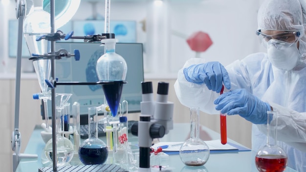 Microbiologist researcher with ppe equipment working with medical transparent glassware analyzing blood sample developing vaccine against coronavirus in hospital laboratory. Medicine concept