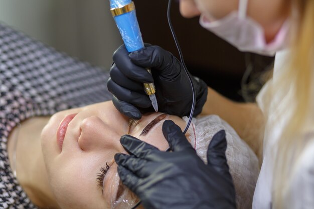 Microblading eyebrows work flow in a beauty salon. Woman having her eye brows tinted. Semi-permanent makeup for eyebrows. Focus on model's face and eyebrow