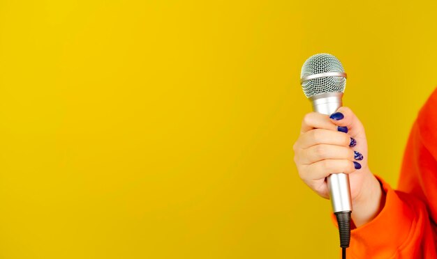 Microphone in woman's hand on yellow background with space for text Unrecognizable woman holding mic for singing