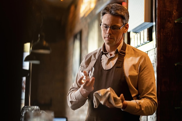 Mid adult barista cleaning drinking glass while working behind bar counter