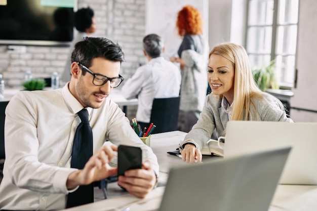 Mid adult businesswoman smiling while her male colleague is showing something on smart phone to her