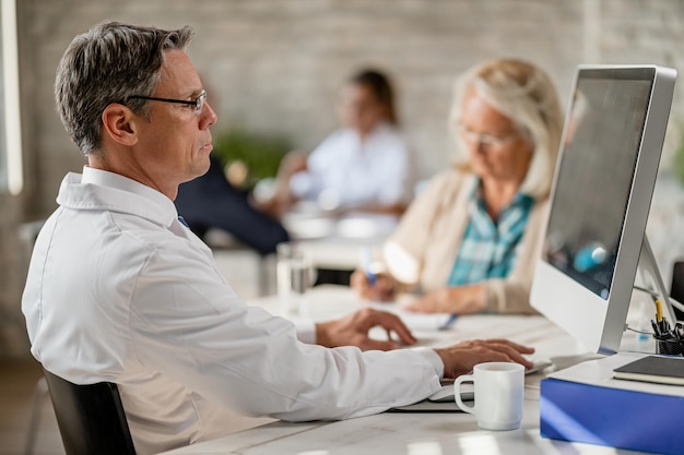 Mid adult doctor using computer and reading medical data of his senior patient during counselling at clinic