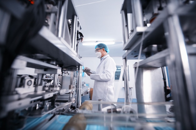 Mid adult male engineer examining machine part on a production line in a factory.