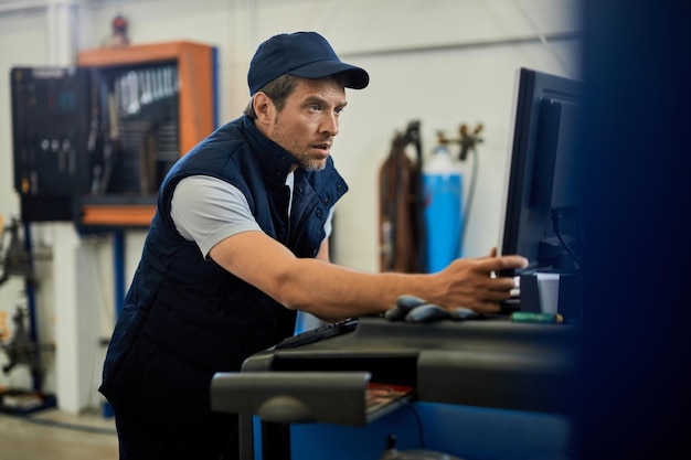 Mid adult mechanic using computer while working in auto repair shop