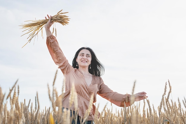 Mid adult woman in beige shirt standing on a wheat field with sunrise on the background back view