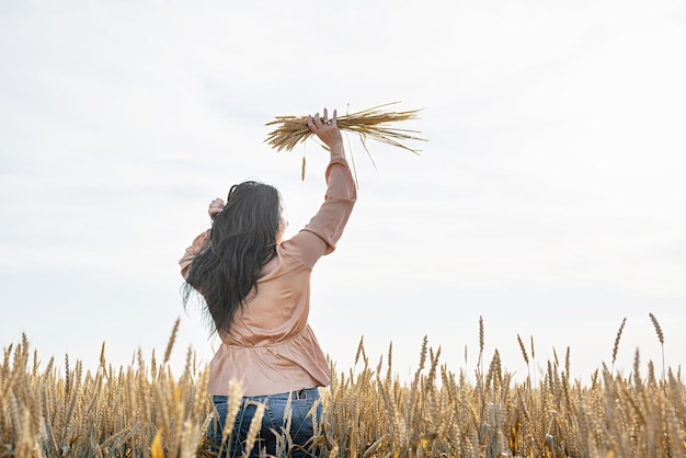 Mid adult woman in beige shirt standing on a wheat field with sunrise on the background back view