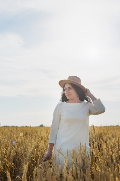 Mid adult woman in white dress standing on a wheat field with sunrise on the background back view