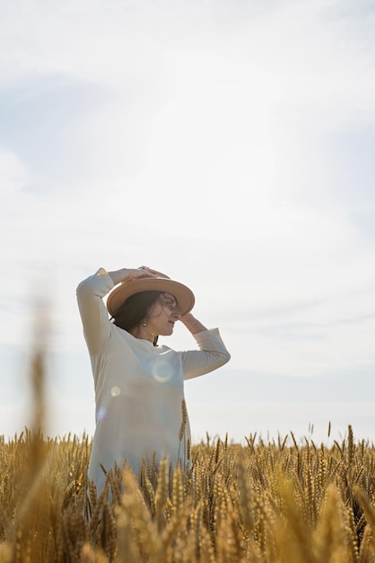 Mid adult woman in white dress standing on a wheat field with sunrise on the background back view