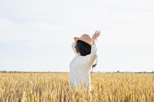 Mid adult woman in white dress standing on a wheat field with sunrise on the background back view