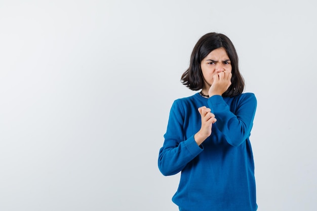 Mid cut hair teenager girl in blue sweater put hand on chin and distracted isolated on white background