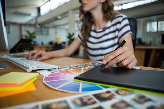 Mid section of female graphic designer using graphics tablet at desk