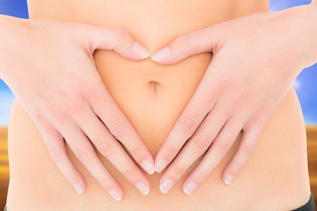 Mid section of a fit woman with hands over belly against sunny brown landscape