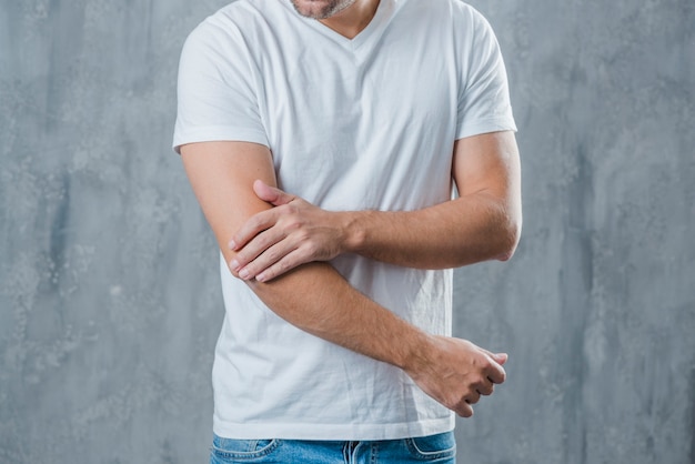 Mid section of a man having elbow pain standing against grey background