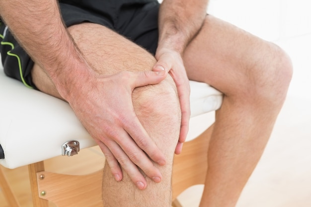 Mid section of a man with his hands on a painful knee