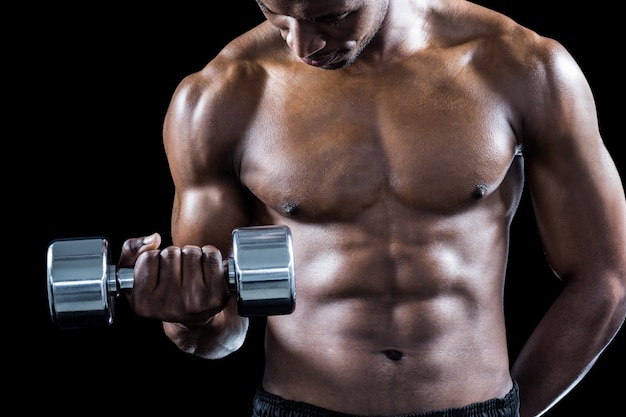 Mid section of muscular athlete exercising with dumbbell