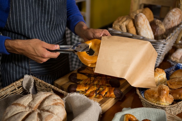 Mid section of staff packing croissant in paper bag at counter