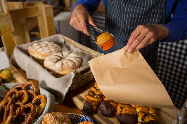 Mid section of staff packing cup cake in paper bag at counter