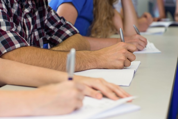 Mid section of students writing notes in classroom