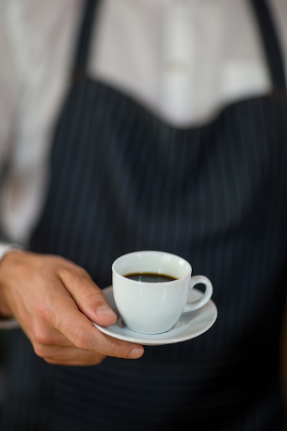 Mid-section of waiter standing with cup of coffee