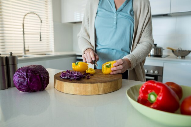 Mid section of woman cutting yellow bell pepper in kitchen