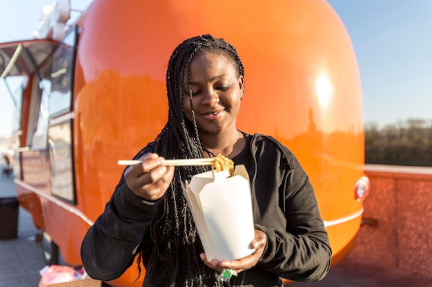 Mid shot woman eating chinese food near food truck