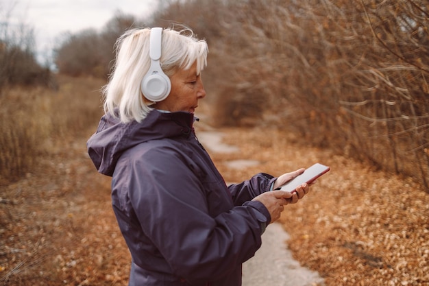 Middle age beautiful woman listening to music using headphones in the city autumn park.