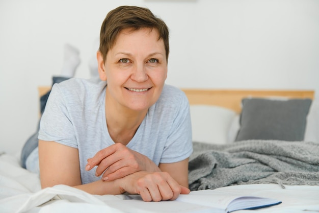 Middle age blonde woman reading book lying on the bed at home