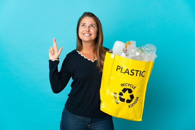 Middle age Brazilian woman holding a bag full of plastic bottles