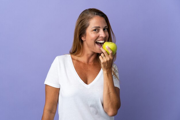 Middle age brazilian woman isolated on purple wall eating an apple