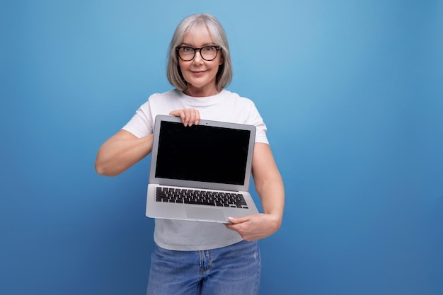 Middle age business mature lady with gray hair masters laptop technique on studio background with