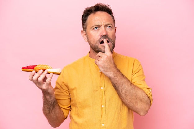 Middle age Caucasian man holding sashimi isolated on pink background having doubts while looking up