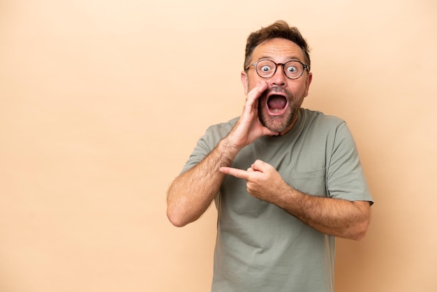 Middle age caucasian man isolated on beige background pointing to the side to present a product and whispering something